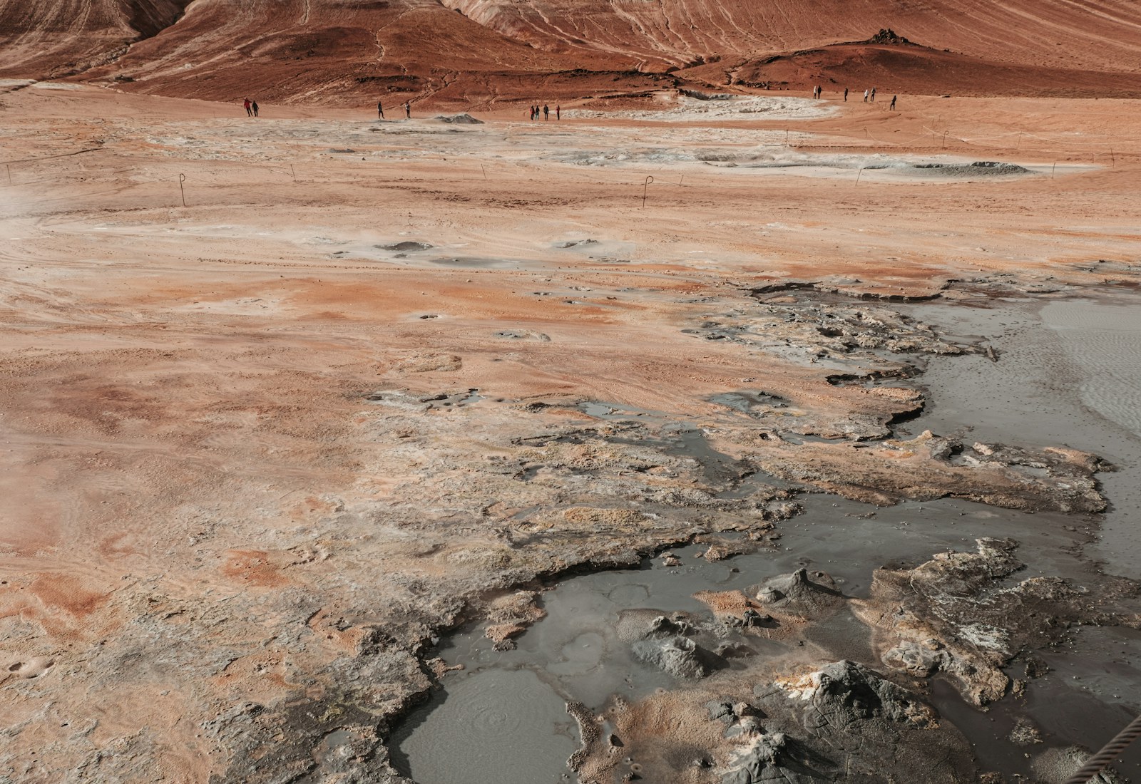 Walkers crossing the mineral-coloured geothermal landscape at Hverir in Iceland